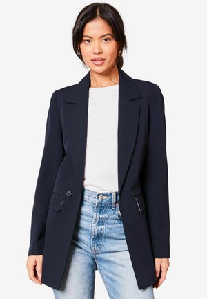 Námořnický blazer se strukturovaným designem, s klopami, dvěma knoflíky a kapsami s klopou, v kombineci s bílým topem a světle modrými džíny.