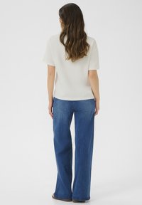Löst sittande ljusbeige topp med korta ärmar, i kombination med vida mörkblå denimjeans. Slät textur, avslappnad design.
