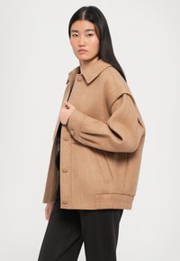 Barna gyapjú keverék kabát széles gallérral, oversized szabással és nagy gombokkal, oldalzsebekkel és texturált anyaggal.