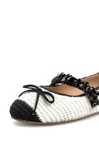 Ballerina con parte superiore intrecciata bianca e accenti neri sulla punta e sul tallone, decorata con una cintura nera gioiello e un fiocco centrale.