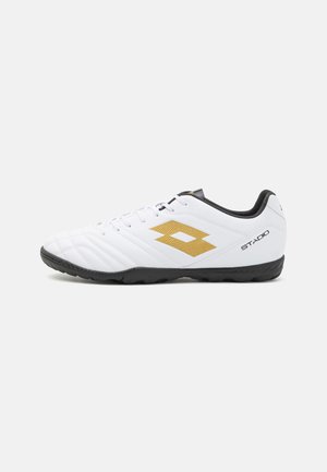 Weißer Fußballschuh mit schwarzer Sohle und Innenfutter, mit goldenem Logo und dem Schriftzug „STADIO“ an der Seite.