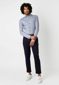 Hellblaues Hemd mit kleinen dunkelblauen Punkte, Slim Fit, langärmlig und schwarzen Knöpfen. Kombiniert mit dunklen Hosen und weißen Sneakers.