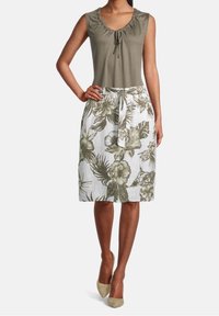 Olivi vihreä hihaton toppi kootulla kaula-aukolla; valkoinen hame, jossa on vihreä kukkakuosi ja nauhavyötärö. Yhdistetty vaaleanbeigeihin korkokenkiin.