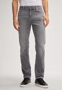 Jeans in denim grigio con taglio dritto, cinque tasche e dettagli di scoloritura discreti. Abbinati a sneakers nere, con una texture complessiva liscia.