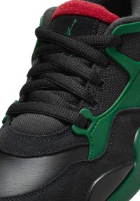 Schwarzer Sneaker mit einer strukturierten Oberseite und grünen Akzenten. Die Zunge ist rot, mit schwarzen Schnürsenkeln und einem glatten Lederzehenbereich.