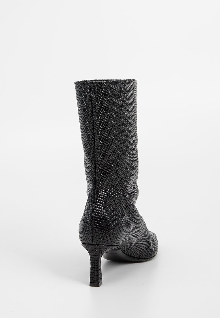 Schwarze Stiefelette bis zur Mitte der Waden mit strukturiertem Muster, spitzem Schuhvorm, und schlankem, mittelhohem Absatz, von hinten auf weißem Hintergrund gezeigt.