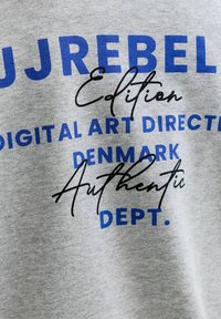 Tissu gris avec texte bleu et noir indiquant « U J REBEL Edition Digital Art Director Denmark Authentic Dept. »
