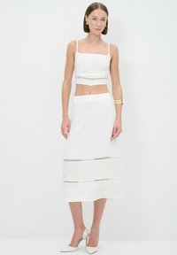 Weißes Zweiteiler-Outfit mit einem zugeschnittenen Oberteil im quadratischen Ausschnitt und Cut-out-Details, kombiniert mit einem passenden Midirock.
