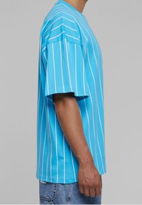 Henkilö, joka pukeutuu löysään taivaansiniseksi T-paitaan, jossa on valkoisia pystyraitoja, yhdistettynä vaaleansinisiin farkkuihin, esitettynä sivuprofiilista.