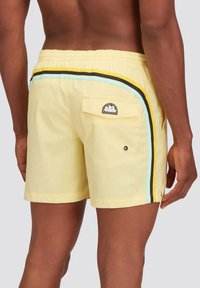 Pantaloni da piscina gialli con strisce laterali nere, blu e gialle, vita elasticizzata e tasca posteriore con una patch del logo.