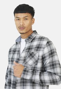 Flanellen shirt in zwart-wit ruitpatroon met een button-down kraag, een enkele borstzak en grijze denim accenten op de kraag.
