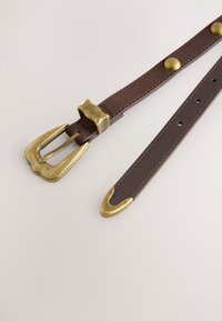 Ceinture en cuir marron avec une boucle en laiton, une pointe arrondie et des rivets assortis. Texture lisse avec un design classique.