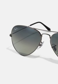 Ochelari de soare Ray-Ban tip aviator cu lentile gri degradé, cadru metalic subțire și accente negre pe brate. Dispune de pad-uri nazale ajustabile pentru confort.