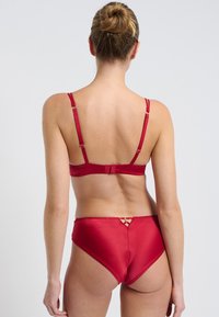 Ensemble de lingerie en satin rouge avec des bretelles ajustables, une fermeture à crochet et un accent décoratif en or à l'arrière du slip. Texture lisse.