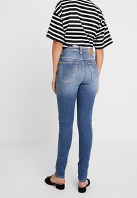 Modré skinny džíny s vybledlým efektem, střední výška pasu, dvě zadní kapsy a hnědá kožená nášivka na pásku. Doplněno pruhovaným topem.