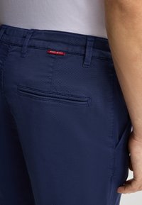 Pantaloni blu navy in tessuto texturizzato, dotati di una tasca posteriore e di un'etichetta rossa con il marchio "JOOP! JEANS". Design strutturato con passanti per cintura.