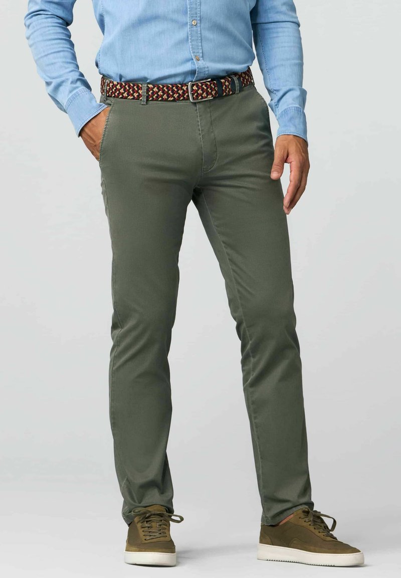 Grüne Chinos aus Baumwolle mit schlanker Passform, ausgestattet mit Seitentaschen und einem gemusterten Woven-Gürtel. Kombiniert mit braunen Sneakern und einem hellblauen Hemd.