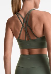 Olivno zelena športna modrca z prečnimi trakovi, narejena iz gladkega blaga, z minimalnim blagovnim znamčenjem na hrbtu.