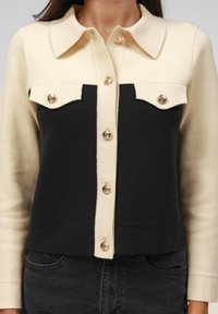 Gebreide cardigan met een gesplitst ontwerp in crème en zwart, met een knoopsluiting aan de voorzijde, twee borstzakken en knopen in goudkleur.