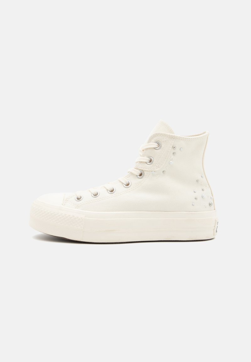 Λευκά καμβά αθλητικά παπούτσια υψηλής κορυφής με υφή στο καουτσούκ σόλες, μεταλλικές οπές και διακοσμητικά τρουκς στο πλάι. Ισιωμένα κορδόνια και στρογγυλή μύτη.