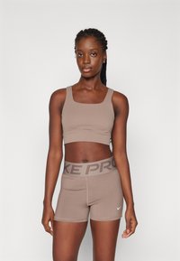 Conjunto de sujetador deportivo y pantalones cortos marrón. El sujetador tiene tirantes gruesos; los pantalones cortos cuentan con una cinturilla elástica de marca en un tono más oscuro. Tejido elástico y suave.