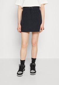 Svart, lätt kjol med elastisk midja och justerbar dragsko. Kombinerad med svarta och grå högskor och svarta strumpor.