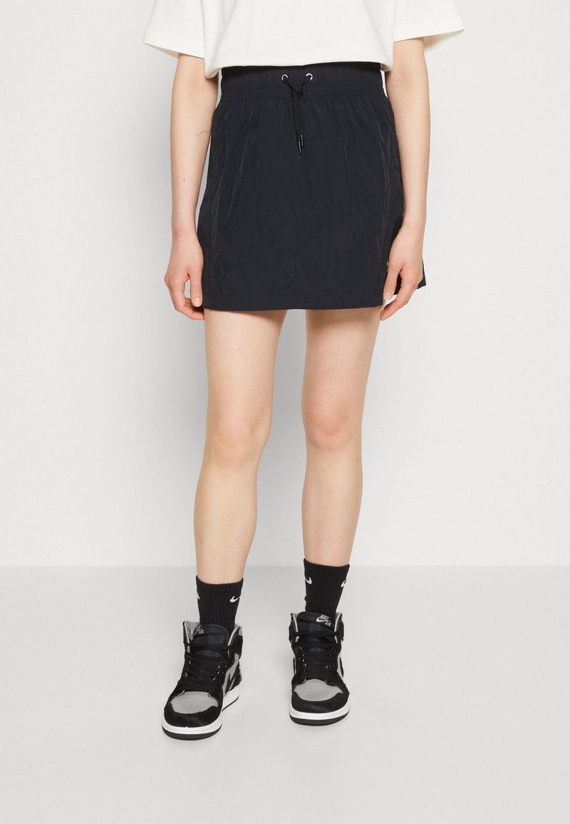 Svart, lätt kjol med elastisk midja och justerbar dragsko. Kombinerad med svarta och grå högskor och svarta strumpor.