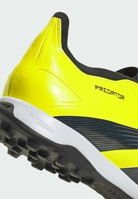 Crampon de football jaune vif avec une finition lisse et brillante, des accents noirs, des motifs texturés et une semelle blanche dotée d'une semelle crantée prononcée.