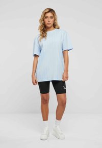 Helles blau gestreiftes, oversized T-Shirt mit kurzen Ärmeln, kombiniert mit schwarzen Radshorts und weißen Sneakers. Schlichtes Design, lässige Passform.