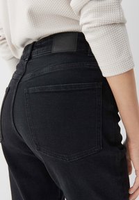 Black denim jeans shown from the back, featuring two rear pockets and a leather patch at the waistband. The fabric has a smooth texture.