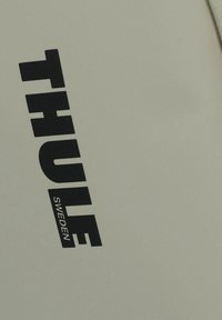 Prodotto Thule di colore grigio chiaro con grande logo nero. Superficie liscia con minima texture, design angolato e dettagli di branding chiari.