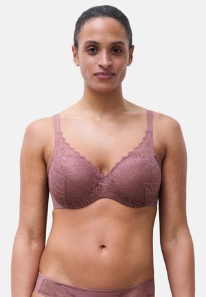 Kvinde iført matchende malva blonde-bh og trusser, der vender fremad mod en ensartet lys baggrund.