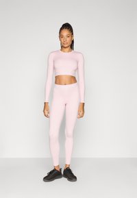 Crop top à manches longues rose clair et leggings taille haute assortis, en matériau lisse et extensible, assortis à des chaussures de sport noires.