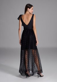 Robe noire avec un corsage ajusté et une jupe semi-transparente ornée d'un motif à pois. Elle présente un dos en V et un accent en ruban sur le côté.