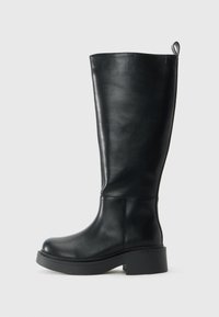 Aukštas juodas odinis botas su kilpike viršuje, apvaliu pirštu ir storu žemu kulnu priešais paprastą baltą foną.