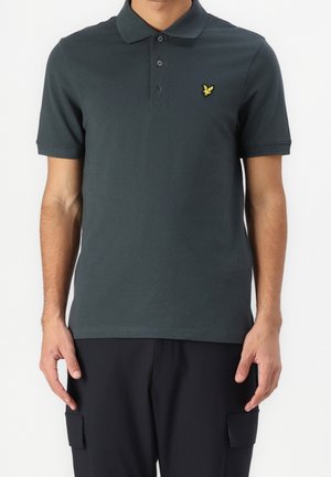 Dark green polo shirt made of cotton, featuring a three-button placket and a small yellow eagle logo on the left chest. Short sleeves.