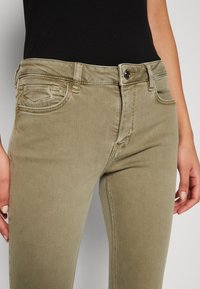 Khaki barvy skinny džíny vyrobené z jemného denimu, se zapínáním na knoflík vpředu, poutky na opasek a přišitými kapsami. Hladký povrch.