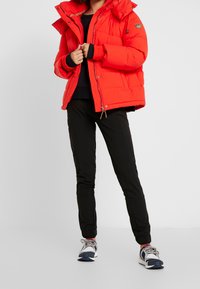 Czerwona puchowa kurtka z kapturem, z zamkiem błyskawicznym i zatrzaskami. Czarne spodnie z elastycznymi mankietami, w połączeniu z wielokolorowymi butami sportowymi.