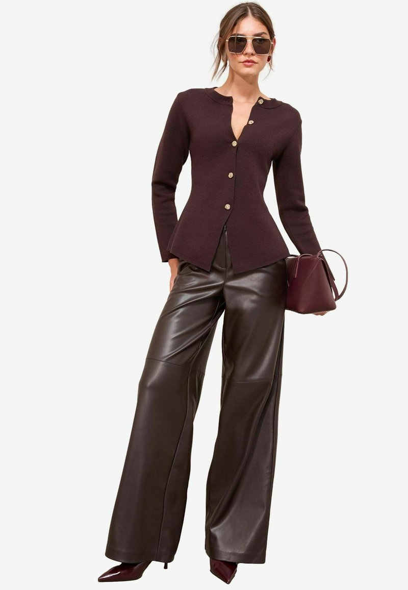 Burgundia kinnitatud kardigan kuldsete nuppudega, koos kõrge vöökohaga pruuni nahast laiade pükstega ja sobiva käekotiga.
