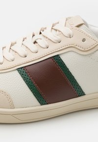 Sneaker in pelle bianca con strisce marroni e verdi. Presenta accenti testurizzati, chiusura con lacci e una suola in gomma liscia.