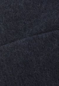Tissu en laine foncée avec une surface douce et texturée, présentant un mélange de fibres foncées et claires créant un motif subtil.