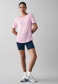Lyserød kortærmet top med et subtilt teksturmønster, parret med navy cykelshorts. Model iført grå sneakers med hvide detaljer.