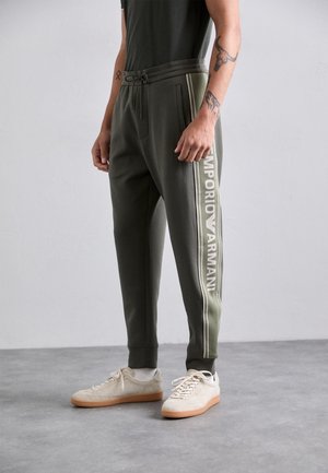 Olive green joggers with a drawstring waist, tapered fit, and white "Emporio Armani" logo along the side. Soft fabric with side pockets.