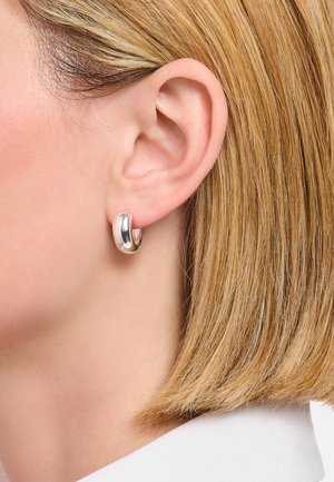 Silberne Creole mit polierter Oberfläche, kreisförmiger Form, glatter Textur und nahtlosem Verschlussdesign, die am linken Ohr getragen wird.