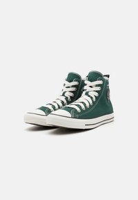 Πράσινα παντόφλες υψηλής κορυφής από καμβά με λευκές καουτσούκ σόλες, στρογγυλή μύτη και κορδόνια. Περιλαμβάνει λογότυπο και αντίθετη λεπτομέρεια ραφής.