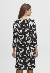 Mönstrad klänning med lång ärm i svart, creme och brunt. Har en abstrakt design, rund halsringning och lätt rynkning vid axlarna.