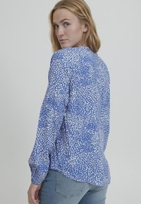 Camicia blu a maniche lunghe realizzata in tessuto leggero, con un motivo astratto a punti bianchi e una vestibilità comoda, con orlo leggermente curvato.