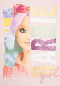 T-shirt rose avec un graphique d'une poupée aux cheveux pastel, de grands yeux bleus et des lunettes de soleil, accompagnée d'un texte scintillant qui dit "fille BARBIE".