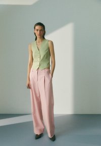 Grønn ermeløs vest med knapper, kombinert med løse rosa bukser. Glatt stoffoverflate, med en tettsittende midje og vide ben.