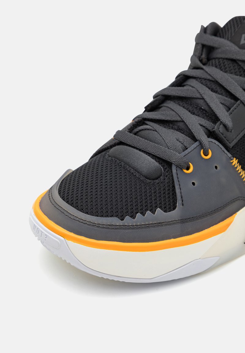 Zapatillas de malla negra con superposiciones texturizadas, acentos grises y una entresuela naranja. Punta redondeada y diseño con cordones, con lengüeta acolchada.